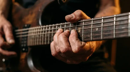 Close-up of a guitarist's fingers executing an expressive string bend on electric guitar neck with dramatic lighting