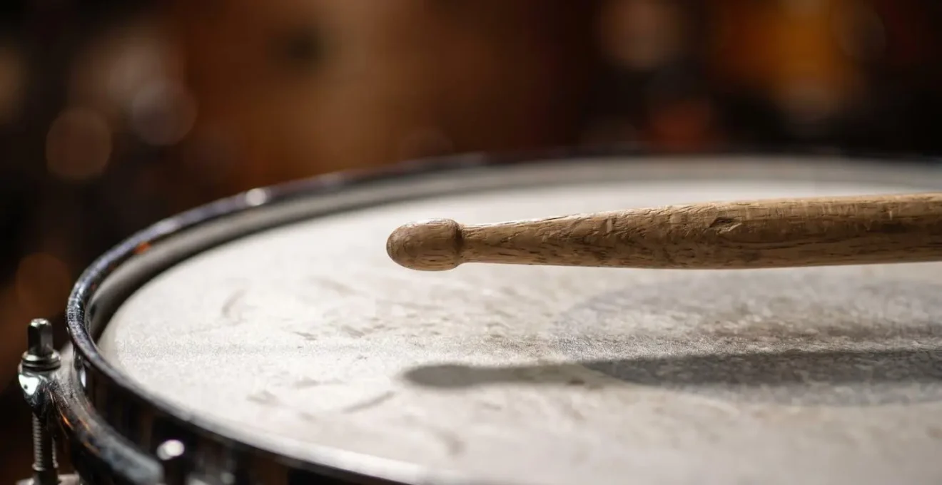Extreme close-up macro photograph of a drumstick hovering just above a snare drum head at the precise 1.5-inch height for ghost note execution