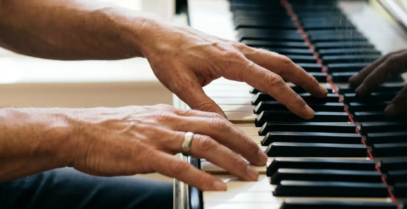 Human hands demonstrating spread voicing technique across wide piano register